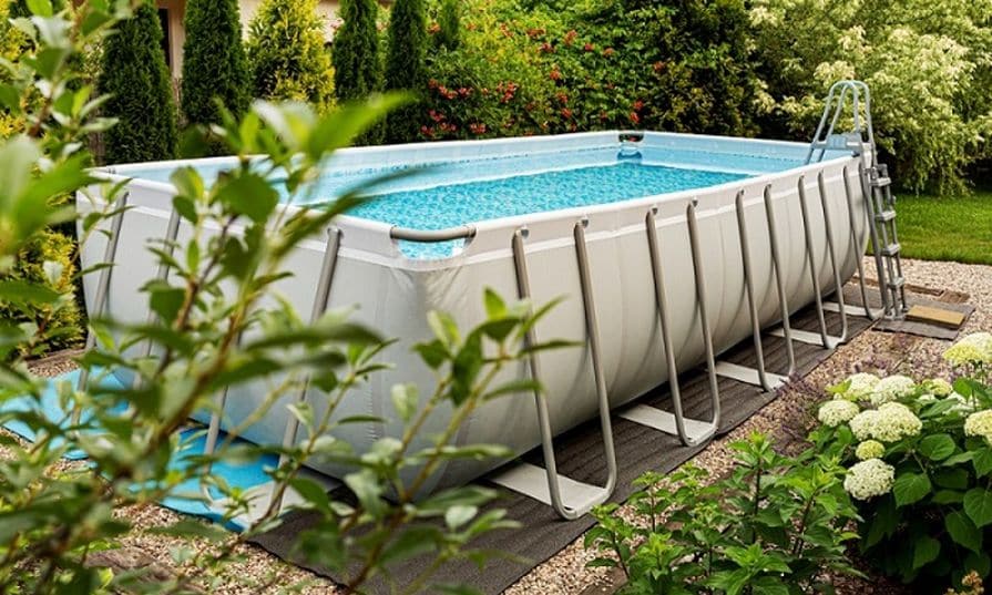 Aufstellpool im Garten mit Leiter und klarem Wasser, umgeben von Pflanzen und Rasen